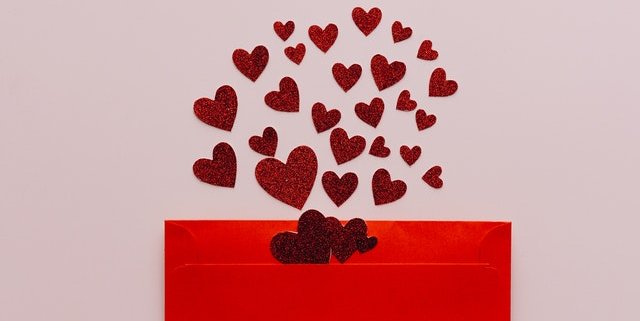 red sparkle hearts spreading out of bright red envelope on pink background