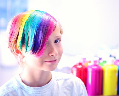 child with multicolored dyed hair with hair dye sitting in background