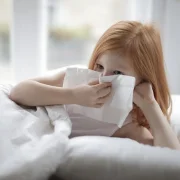 child blowing their nose into a tissue while laying in bed