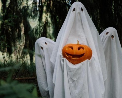 family posing in the woods dressed in ghost costumes and holding a pumpkin